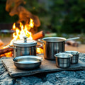 Foldable aluminum camp cookware set arranged on granite slab beside campfire