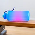 Gradient blue to pink reusable sport water bottle on wooden bench
