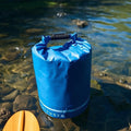 Blue roll-top waterproof dry bag floating in clear river next to kayak paddle