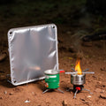 Foldable aluminum wind shield with small camping stove on dirt ground